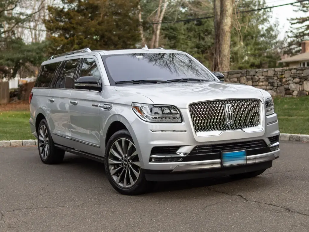 A silver Lincoln Navigator SUV parked on a street with trees in the background.