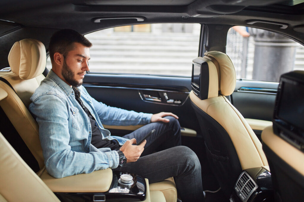 Man in blazer using tablet in car's backseat.