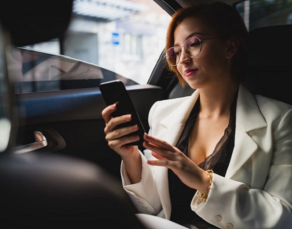 Businesswoman in a white blazer using smartphone inside a car.