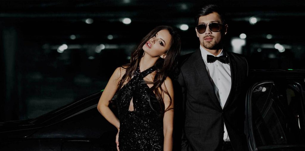 A stylish couple dressed in elegant black evening wear posing confidently.
