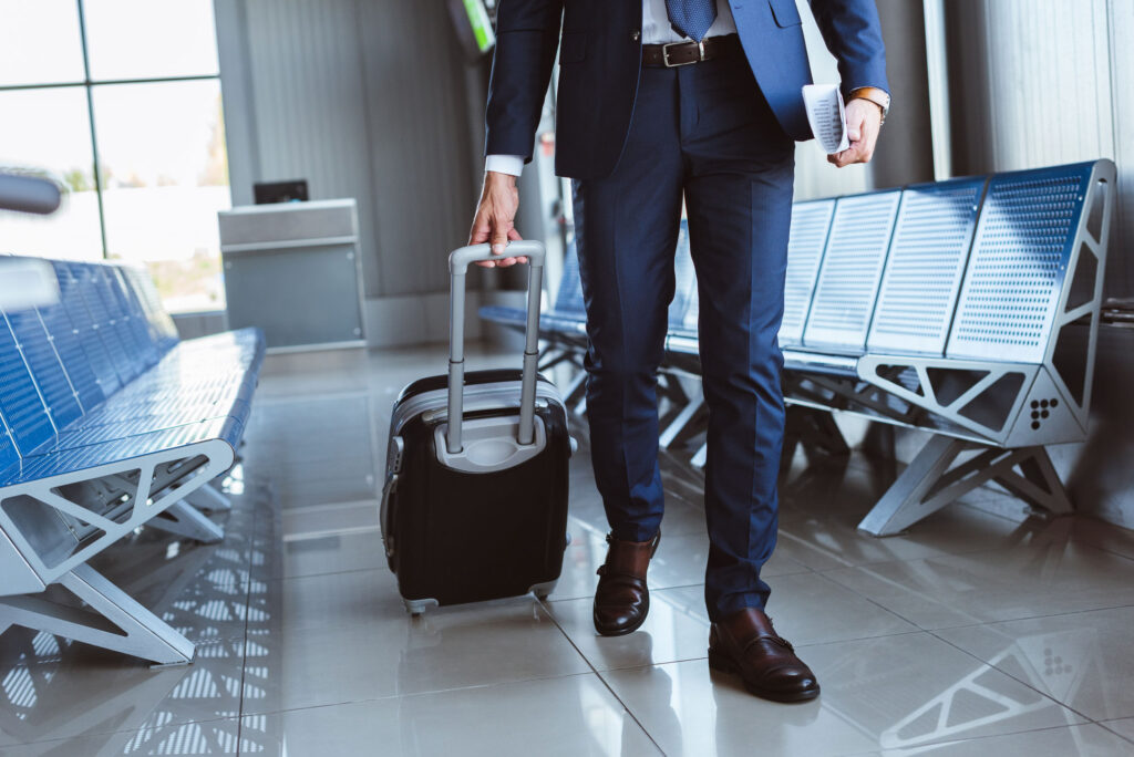 A businessman in a suit with a rolling suitcase at an airport.