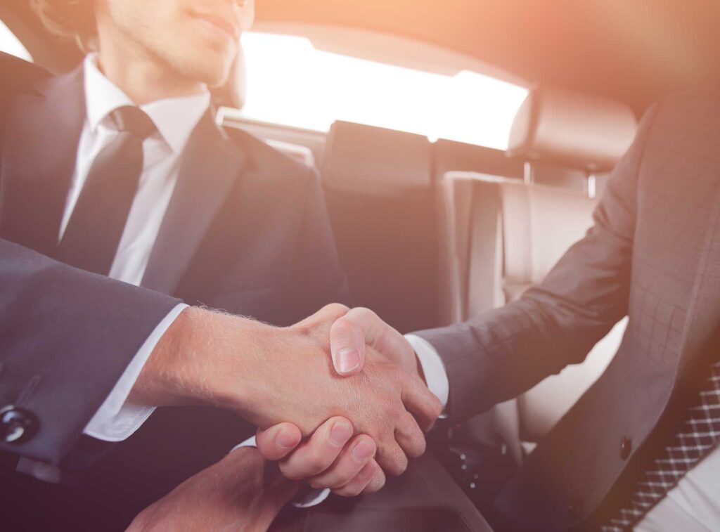 Business professionals shaking hands inside a car.