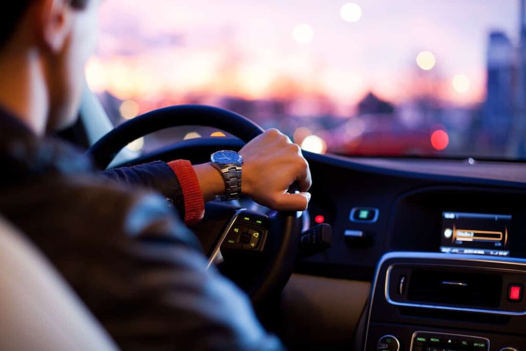 Person driving a car during sunset, hand on the steering wheel.