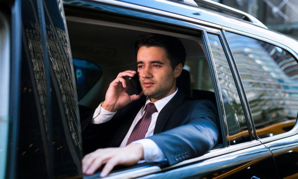 Businessman in suit talking on phone inside a car.